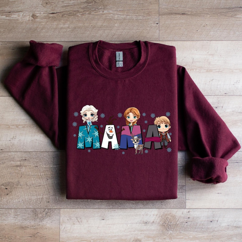 Puede incluir: Sudadera color burdeos con un gr&aacute;fico de los personajes de Frozen, incluyendo Elsa, Anna, Olaf y Kristoff. El gr&aacute;fico dice "MAMA" con cada personaje de pie sobre una letra.