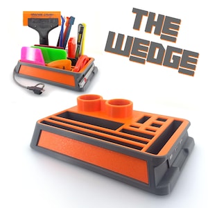 May include: The Wedge is a 3D printed organizer with multiple compartments for tools and supplies. It features a gray base with orange accents and a separate compartment for two tools. The organizer has a label that reads "The Wedge".
