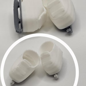 May include: White 3D-printed objects, possibly components or parts, are arranged against a light background. The objects have a cylindrical shape with a rectangular feature on the side and a small, dark gray base.