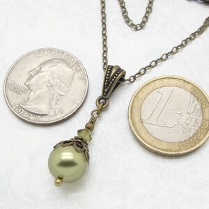 Pode incluir: Colar com pingente em estilo antigo com uma p&eacute;rola verde perolada. O colar tem uma corrente de cor bronze e elementos decorativos. Uma moeda de um euro est&aacute; ao lado do colar como refer&ecirc;ncia de tamanho.
