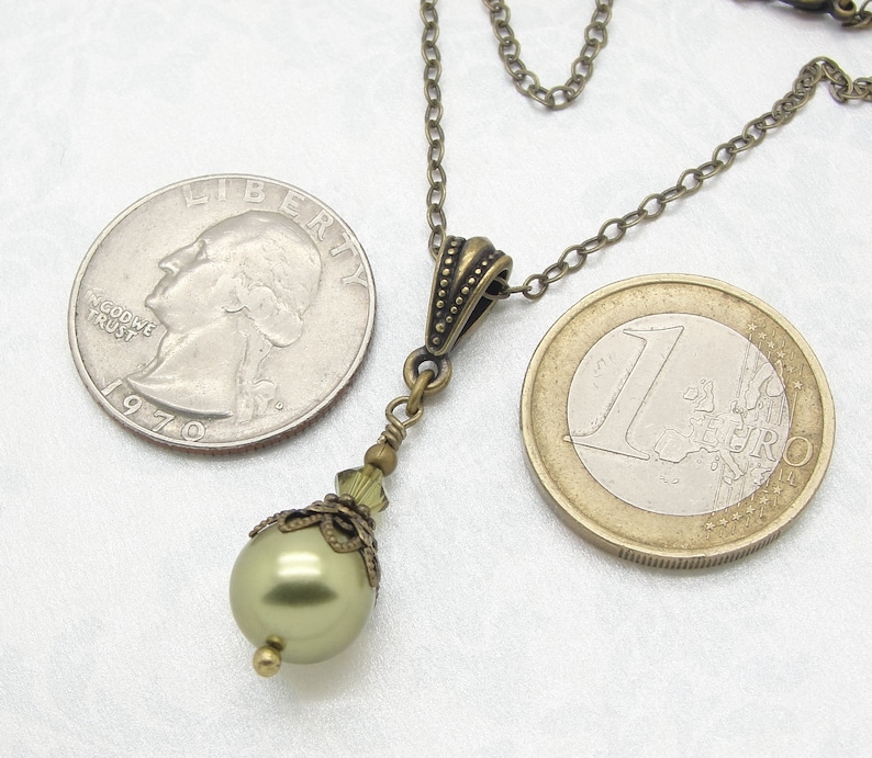 Pode incluir: Colar com pingente em estilo antigo com uma p&eacute;rola verde perolada. O colar tem uma corrente de cor bronze e elementos decorativos. Uma moeda de um euro est&aacute; ao lado do colar como refer&ecirc;ncia de tamanho.