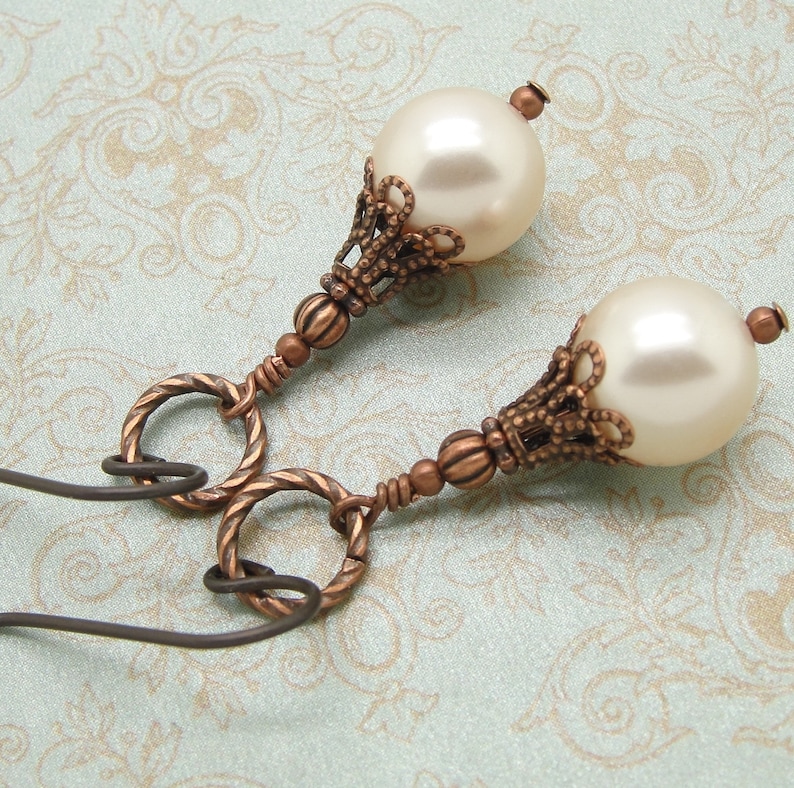 May include: A pair of earrings with a vintage design. Each earring features a white pearl bead with a copper filigree setting and a copper wire loop.