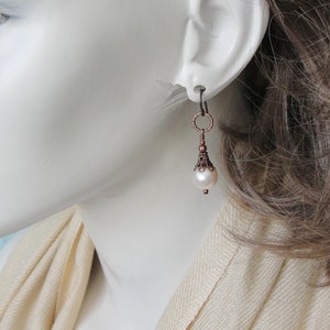 May include: Copper and pearl dangle earrings with a delicate, ornate design. The earrings feature a small, round pearl drop and a copper filigree pendant.