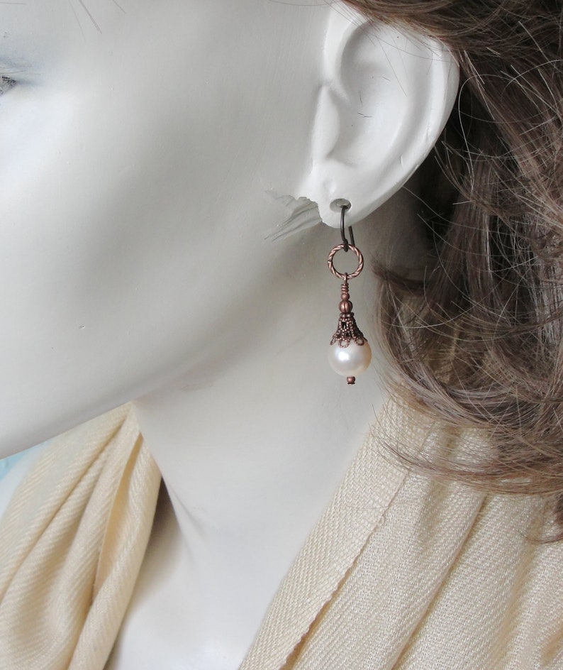May include: Copper and pearl dangle earrings with a delicate, ornate design. The earrings feature a small, round pearl drop and a copper filigree pendant.