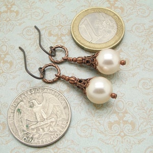 May include: A pair of earrings with a white pearl drop and a copper-toned filigree design. The earrings have a simple wire hook closure.