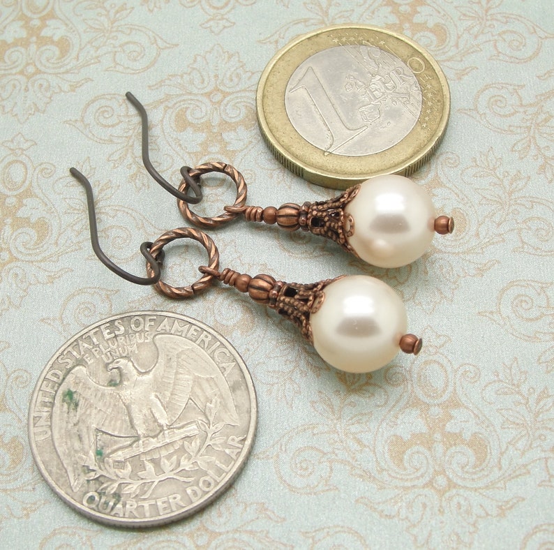 May include: A pair of earrings with a white pearl drop and a copper-toned filigree design. The earrings have a simple wire hook closure.
