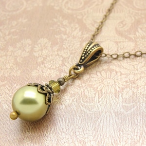 Pode incluir: Um colar com pingente em estilo vintage com uma grande conta verde-oliva perolada. A conta &eacute; acentuada com um trabalho de metal dourado antigo e uma corrente delicada. Uma pe&ccedil;a de joalheria cl&aacute;ssica.