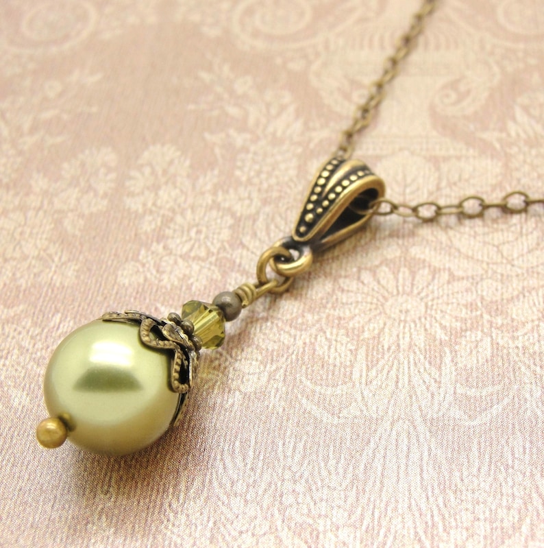 Pode incluir: Um colar com pingente em estilo vintage com uma grande conta verde-oliva perolada. A conta &eacute; acentuada com um trabalho de metal dourado antigo e uma corrente delicada. Uma pe&ccedil;a de joalheria cl&aacute;ssica.