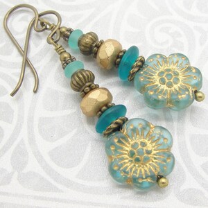 May include: Teal and gold dangle earrings with a floral design. The earrings feature a mix of glass and metal beads.