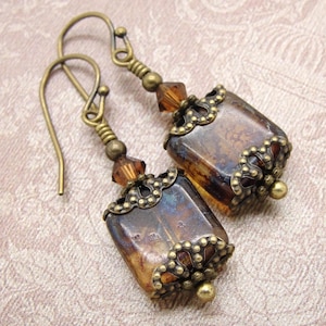 May include: A pair of vintage earrings featuring rectangular, amber-coloured glass stones. The earrings have ornate, antique brass-toned metalwork, including decorative caps and ear wires. Small, faceted amber beads accent the design.