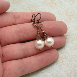 May include: A pair of dangle earrings with a white pearl drop and a bronze filigree design.