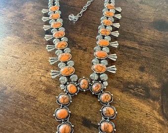 Könnte beinhalten: Eine Halskette im Squash-Blossom-Stil mit ovalen, orangefarbenen Steinen mit dunkler Maserung, die in silberfarbenes Metall gefasst sind. Das Schmuckstück besteht aus einer Reihe runder Silberperlen und einer Metallkette mit Karabinerverschluss.