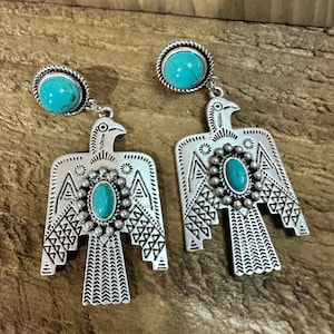 May include: Silver earrings with turquoise stones and a bird design. The earrings have a post back and a detailed, textured finish. The bird's wings and body are intricately designed with geometric patterns. The earrings are approximately 5 cm in length.