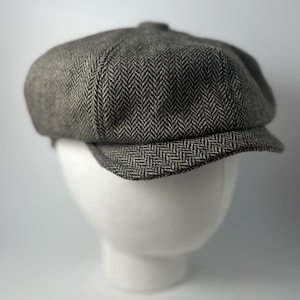 May include: A gray and black herringbone patterned newsboy cap.