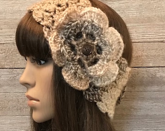 May include: A crocheted headband in beige and brown tones, adorned with a large, three-dimensional flower with a button centre. The headband has a textured stitch pattern, and the flower provides a decorative element to the accessory.