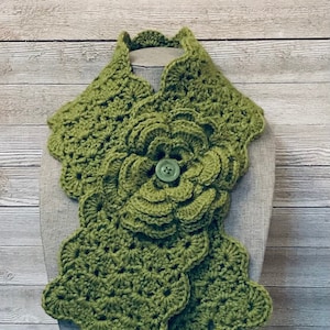 May include: A green crocheted cowl with a large flower design and a green button in the center.