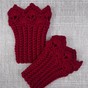 May include: A pair of handmade, dark red crochet wrist cuffs. The cuffs have a ribbed design on the lower portion and a decorative, scalloped edge. The cuffs are displayed on a textured, gray background.