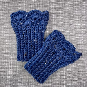 May include: A pair of dark blue crochet wrist warmers. The wrist warmers have a scalloped edge and a ribbed design. The yarn has flecks of white and brown. The wrist warmers are displayed on a grey textured surface.