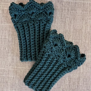 May include: A pair of dark teal crochet fingerless gloves featuring a ribbed texture on the main body and a decorative scalloped edge at the top. The yarn work displays a consistent stitch pattern throughout both pieces, showcasing a deep green hue.