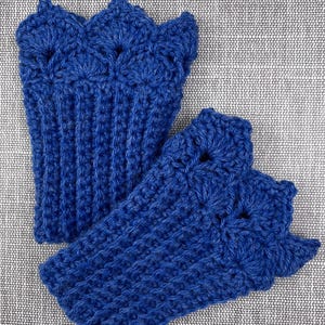Può includere: Due guanti senza dita all'uncinetto blu reale fatti a mano. I guanti hanno un bordo smerlato e un design a coste strutturato. Sono esposti su una superficie grigia strutturata.