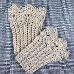 May include: A pair of beige crochet fingerless gloves. The gloves feature a ribbed design on the wrist and a decorative scalloped edge. The open-finger design allows for dexterity while keeping hands warm.