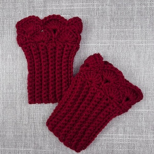 May include: Two burgundy crochet wrist warmers. The wrist warmers are made of a ribbed knit pattern and have a scalloped edge. The items are displayed on a gray textured surface.