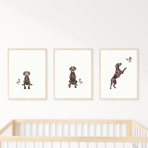 Può includere: Set di tre stampe incorniciate con illustrazioni di cani. I cani sono raffigurati in varie pose, con anatre. Le cornici hanno una finitura in legno chiaro. L'opera d'arte è ambientata su uno sfondo bianco.