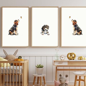 May include: Three watercolour paintings of a beagle puppy looking up at a butterfly. The puppy is brown, black, and white. The butterfly is yellow. The paintings are framed in light wood frames and are hanging on a white wall.