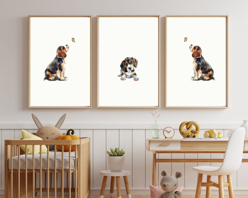 May include: Three watercolour paintings of a beagle puppy looking up at a butterfly. The puppy is brown, black, and white. The butterfly is yellow. The paintings are framed in light wood frames and are hanging on a white wall.