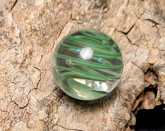 May include: A green glass marble with a swirling pattern inside. The marble is clear and has a light green colour.
