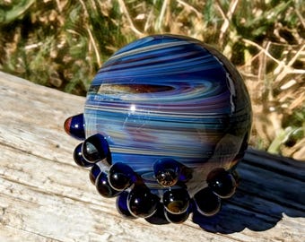 Peut inclure: Une boule de verre bleue et violette avec un motif tourbillonnant et une base de bulles de verre bleu foncé.