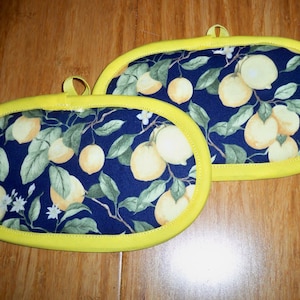 May include: Two yellow lemon-themed oven mitts with a dark blue background and a yellow trim.