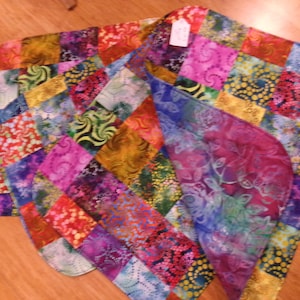 May include: A set of colourful, quilted placemats with a patchwork design. The placemats feature a variety of vibrant colours and patterns, including pink, blue, yellow, and green. The edges are rounded, and a tag is attached to one of the placemats.