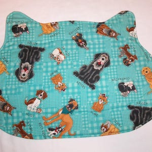 May include: A turquoise, cat-shaped pet placemat with a repeating pattern of various dog breeds. The dogs are in different poses and colors, with words like "Kisses", "Family", and "Adopt" scattered throughout the design.