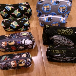 Puede incluir: Una colección de bolsas con cremallera con temática de Star Wars en varios tamaños. Los diseños incluyen a Baby Yoda, retratos de personajes y naves espaciales sobre fondos negros, grises y estampados. Cada bolsa tiene una cremallera negra.