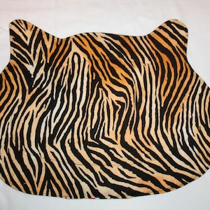 May include: A decorative mat in the shape of a cat's head, featuring a bold tiger stripe pattern in black and orange. The mat has rounded edges and two pointed ear shapes at the top.