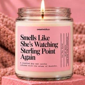 May include: A clear glass jar candle with a lit wick and white wax. The pink label features the text: sweetwickco, Smells Like She's Watching Sterling Point Again, Soy Wax Blend, 50-60 Hours, Keep Away From Flammables, A scented Soy wax candle infused with the aroma of Muskoka.