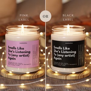Puede incluir: Dos velas en frasco de vidrio con cera de soja, una con etiqueta rosa y otra con etiqueta negra. Ambas etiquetas muestran el texto: Smells Like She's Listening To (any artist) Again, sweetwickco, A Scented Soy Wax Candle, Infused With The Aroma Of Therapeutic Music In Every Flame.