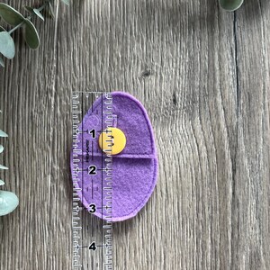 Op de afbeelding: Een paarse felt pouch met een gele knoopsluiting. De pouch is ongeveer 7,6 cm hoog.