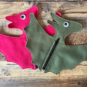 May include: Two felt dinosaur costumes, one pink and one green, with large white eyes and a black zipper on the green costume.