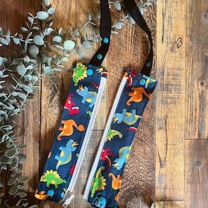 May include: A pair of black fabric straps with blue and white dinosaur print fabric pouches attached. The pouches have zippers and blue snap buttons on the straps.