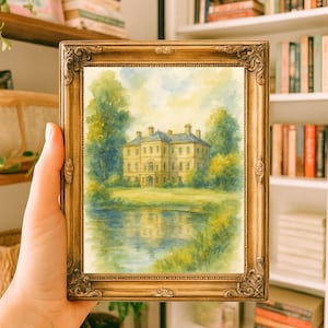 May include: A framed watercolor painting of a stately yellow mansion with a blue roof, reflected in a calm lake. The painting is set in a gold ornate frame. The artwork is held in a person's hand.