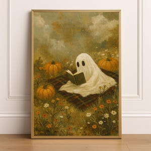 May include: A framed print depicts a whimsical scene of a ghost reading a book in a field. The ghost is draped in a white sheet, sitting on a plaid blanket, surrounded by pumpkins and wildflowers. The artwork has a vintage, autumnal feel.