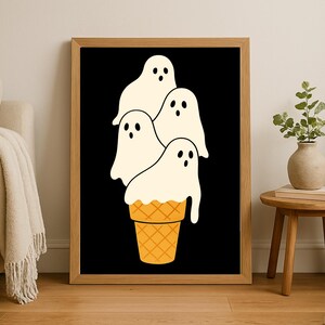 May include: A framed art print featuring a whimsical illustration of four white ghost figures stacked on top of a waffle cone. The background is black, and the cone is orange. The artwork is displayed in a wooden frame.