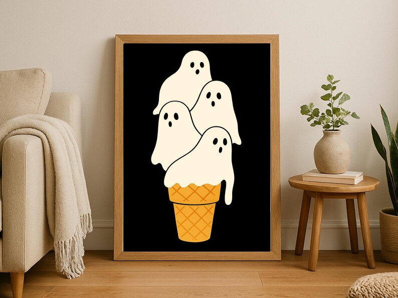 May include: A framed art print featuring a whimsical illustration of four white ghost figures stacked on top of a waffle cone. The background is black, and the cone is orange. The artwork is displayed in a wooden frame.