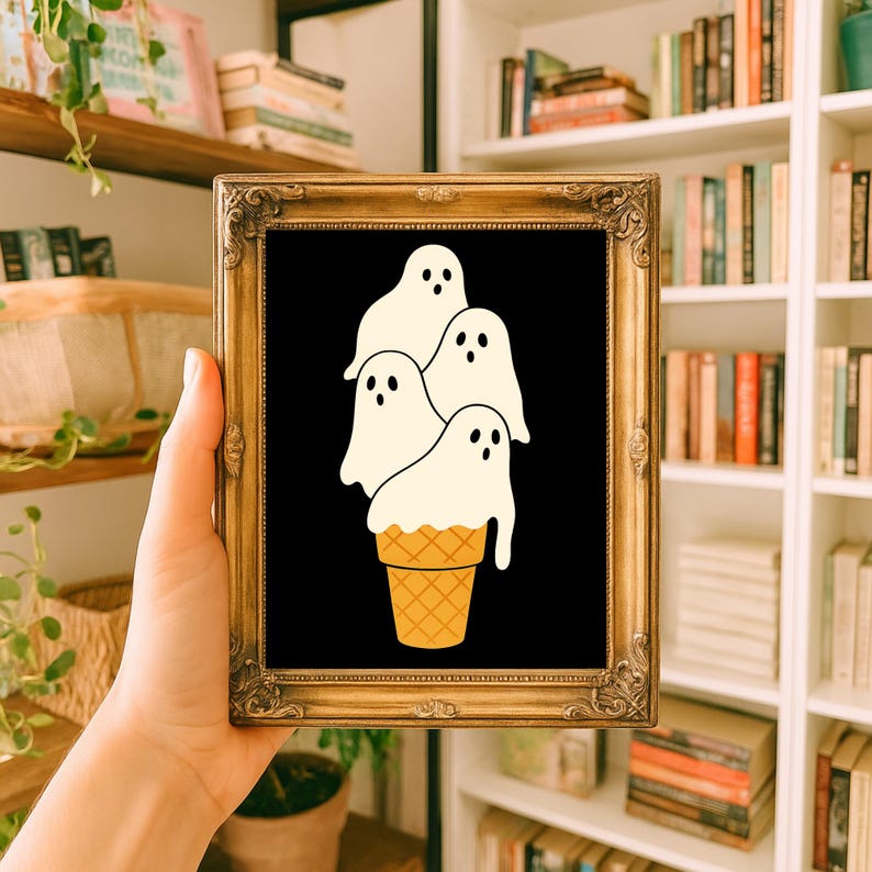 May include: A framed art print featuring a whimsical design of four white ghost figures resembling ice cream scoops atop a waffle cone. The artwork is set against a black background within a gold ornate frame, perfect for Halloween decor.