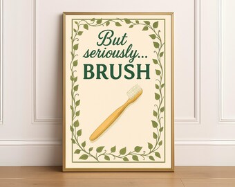 May include: Framed print with the text "But seriously... BRUSH" in dark green. The image features a wooden toothbrush and a decorative border of green leaves. The background is a light beige color.