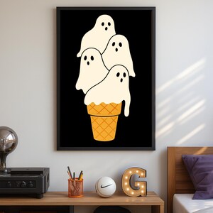 May include: A framed art print featuring a whimsical illustration of four ghost figures resembling ice cream scoops atop a waffle cone. The ghosts are white with black eyes and the cone is orange. The background is black.