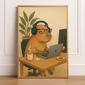 May include: Framed art print showing a capybara wearing glasses and headphones, working on a laptop. A coffee cup, sticky note, and biscuit are on the desk. A plant and computer monitor are also visible.