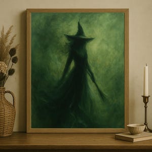 May include: Framed artwork featuring a silhouetted witch figure in a flowing gown and hat against a green, smoky background. The artwork is in a wooden frame, displayed on a wooden surface with decorative elements.
